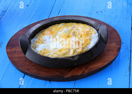 Eine traditionelle Mahlzeit mit Rührei im rustikalen Container gebraten auf einem blauen Holztisch. Stockfoto