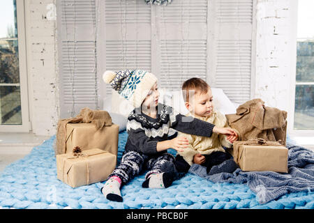 Thema Weihnachten Morgen. Zwei untergeordnete Kaukasischen Junge und Mädchen Bruder und Schwester sind auf dem Bett zu sitzen in einer Umarmung mit einem Lächeln und Freude sind die Eröffnung neuer Stockfoto