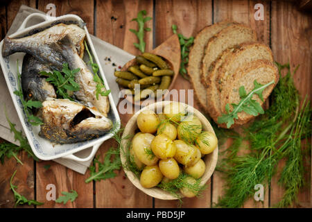 Mittagessen. gebackene Dorado und jungen Kartoffeln. Marinierten Gurken und Schwarzbrot. Im rustikalen Stil, Stockfoto