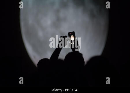 Madrid, Spanien. 27. Juli, 2018. Ein Mann Bilder eine Projektion von einem Blut Mond über Madrid bei einer totalen Mondfinsternis, die längste des Jahrhunderts und zeitgleich mit dem nächsten Ansatz des Mars zur Erde. Während die Eclipse die Sternwarte ('Planetario de Madrid") auf einem großen Bildschirm die totale Sonnenfinsternis Mond projiziert hat, in Madrid, Spanien. Credit: Marcos del Mazo/Alamy leben Nachrichten Stockfoto