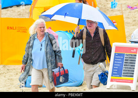 Lyme Regis, Dorset, Großbritannien. 28. Juni 2018. UK Wetter. Urlauber Unterschlupf unter einem Regenschirm verlassen den Strand als der Regen beginnt in den Badeort Lyme Regis am ersten Tag der Hauptversammlung der Stadt RNLI lifeboat Woche an einem kühlen, windigen Tag. Foto: Graham Jagd-/Alamy leben Nachrichten Stockfoto