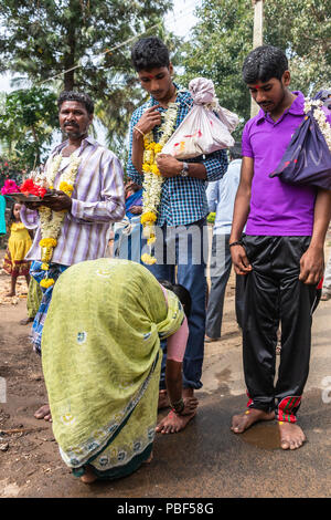 Belathur, Karnataka, Indien - November 1, 2013: Pilgrim erhalten Männer Fuß durch Frau gewaschen während der abschiedszeremonie. Girlanden, Rucksäcke und viel Farbe Stockfoto