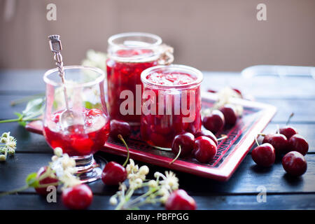 Marmelade aus Kirsche, in Dosen. winter Desserts. Dunkle Foto. Feder weiß blumen Stockfoto