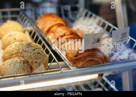 Coffee shop Fenster mit gebackenen Speisen, Gebäck. Closeup makro Gruppe von runden frische Käse Brötchen und Umsätze im Korb mit weißem Papier Stockfoto