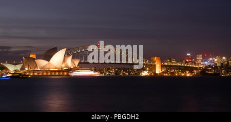 Opera House und die Harbour Bridge in Sydney bei Nacht, Reflexion über Hafen Blick vom Botanischen Garten. Es ist von goldenen Lichter in der Nacht beleuchtete Attr Stockfoto