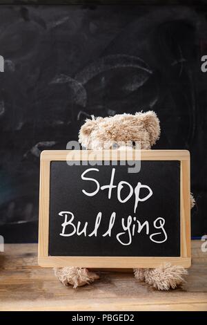 Mobbing in der Schule. Teddybär hinter einer Tafel, stop Mobbing Text auf der Tafel Stockfoto