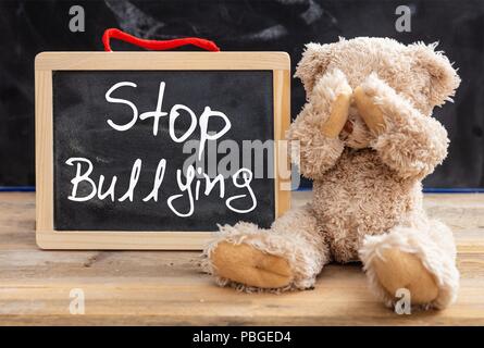 Mobbing in der Schule. Teddy Bär für Augen und Stop Mobbing Text auf einer Tafel Stockfoto