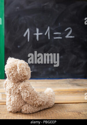 Schule Klasse Math. Teddy Bär auf eine einfache Gleichung auf einer Tafel. Eins plus Eins gleich zwei Stockfoto