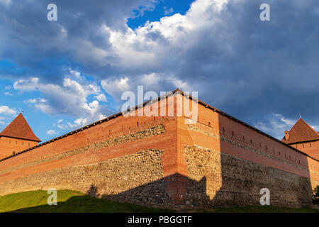 Ein mächtiger Turm der Lida Burg aus rotem Backstein und Stein leuchtet mit der Sonne gegen einen schönen aber stürmischen Himmel, Weißrussland Stockfoto