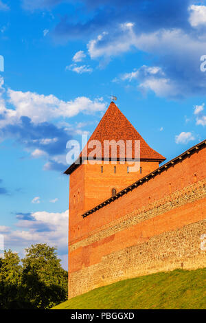 Ein mächtiger Turm der Lida Burg aus rotem Backstein und Stein leuchtet mit der Sonne gegen einen schönen aber stürmischen Himmel, Weißrussland Stockfoto