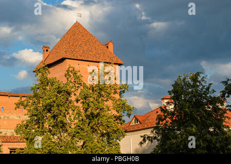 Ein mächtiger Turm der Lida Burg aus rotem Backstein und Stein leuchtet mit der Sonne gegen einen schönen aber stürmischen Himmel, Weißrussland Stockfoto