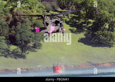 Ein UH-60 Black Hawk Helikopter der Kalifornien Army National Guard schwebt über See Pardee in Ione, Kalifornien, das Sammeln von Wasser in einem Eimer, 14. April 2018, während der WILDLAND Löschübungen, eine kooperative Mission zwischen Cal Guard und die Kalifornien Abteilung der Forstwirtschaft und Brandschutz (CAL). (U.S. Army National Guard Foto: Staff Sgt. Eddie Siguenza) Stockfoto