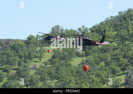 Ein Paar von Kalifornien Army National Guard UH-60 Black Hawk Hubschrauber fliegt über See Pardee in Ione, Kalifornien, nach dem sammeln Wasser, 14. April 2018 und der Überschrift zu einem simulierten wildfire während einer jährlichen Übung zwischen Cal Guard und die Kalifornien Abteilung der Forstwirtschaft und Brandschutz (CAL). (U.S. Army National Guard Foto: Staff Sgt. Eddie Siguenza) Stockfoto