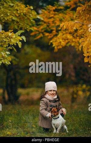 Kind, Mädchen sitzt und spielt mit seinem Hund beim Spaziergang im Wald. Stockfoto