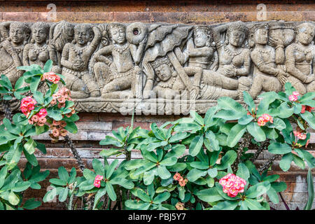 Balinesische steinbildhauerei an der Wand in der Nähe von blühenden Euphorbia milii Anlage. Bali, Indonesien. Stockfoto