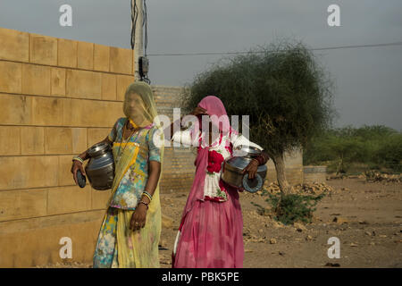 Frauen in ländlichen Gebieten durchzuführen Metall Krüge mit Wasser auf dem Kopf. Wüsten Nationalpark Jaisalmer Indien Juni 2018 Stockfoto