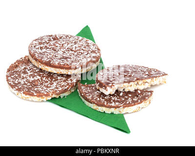 Reis Kuchen, Kekse mit Milch Schokolade und Kokos. Gesunde knackige behandeln, auf grünem Papier Serviette, Servietten, auf weissem isoliert. Stockfoto