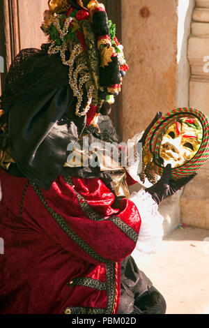 Karneval In Venedig: Piazzetta San Marco, Venedig, Italien. Maskierte Nachtschwärmer posiert mit einem Spiegel unter den Arkaden des Palazzo Ducale Stockfoto