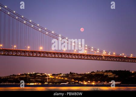 Blick auf die Mondfinsternis, die längste Blut Mond des 21. Jahrhunderts, über die Brücke des 25. April in Lissabon, Portugal Stockfoto