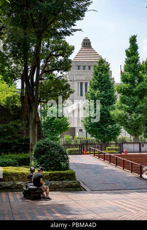 Schüler mit Laptop neben lady Skulptur mit der japanischen Regierung Gebäude Pyramide im Hintergrund sitzen Stockfoto