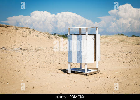 Blau und Weiß Umkleidekabine auf der wilden Griechische Strand, mit geschlossener Tür. Hellen Himmel mit Wolken und goldenen Sand. Stockfoto