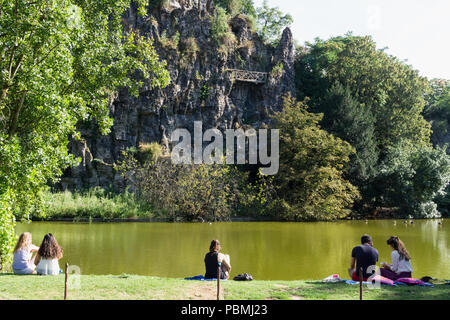 Paris Park mit See - Menschen entspannend in der Nähe der See im Park des Buttes Chaumont in Paris, Frankreich, Europa. Stockfoto
