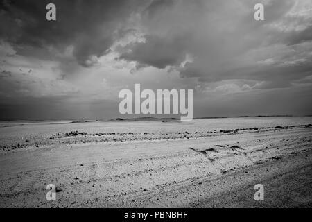 Staubige holprige Straße durch die Wüste von Namibia als Storm clouds Overhead erzeugen kontrastreiche sky Verhaltensmuster zu sammeln Stockfoto