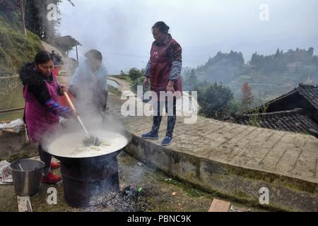 Provinz Guizhou, China - ca. Dezember 2017: Drei Frauen kochen Reis anlässlich der Hochzeit halten außerhalb, hoch in den Bergen von Guizho Stockfoto