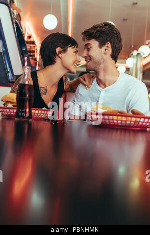 Romantisches Paar speisen in einem Restaurant mit Speisen und alkoholfreie Getränke auf dem Tisch. Lächelnd Mann und Frau teilen ein Pommes Frites es in Ihren zwischen Holding Stockfoto