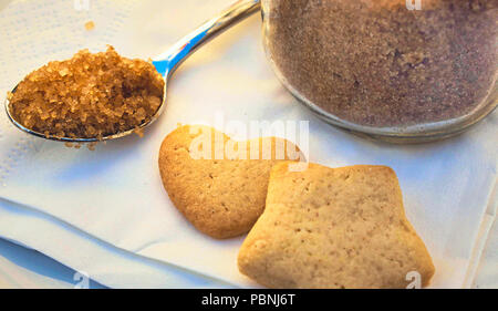 Brauner Zucker in einem Teelöffel für Tee oder Kaffee mit Herz und Stern geformte Gebäck auf einem Tisch in einem Cafe Stockfoto