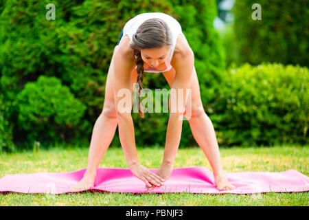 Die ganze Länge der schwangeren Frau vorwärts Yoga Biegung mit Beine auseinander für fit Oberschenkel und Rücken auf die Matte in Park Stockfoto