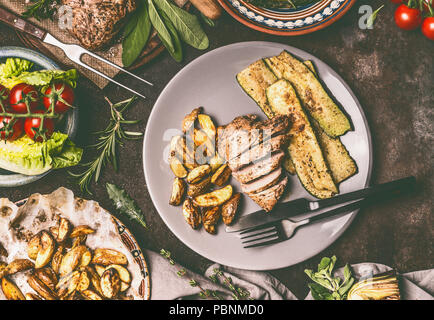 Blick von oben auf die Platte mit gegrilltem Schweinefleisch Steak, Braten und frisches Gemüse und gebackene Kartoffeln, Teller und Besteck auf rustikalen Holztisch. Rustikales Essen Stockfoto