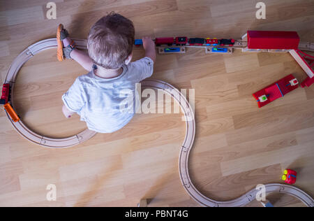 Kind Junge spielt mit hölzernen Spielzeugeisenbahn. Ansicht von oben. Pädagogische Spielwaren Stockfoto