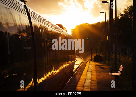 Am späten Nachmittag Sonnenlicht reflektiert aus einem Zug Ankunft am kleinen Bahnhof von Quelle, in der Nähe der Halle (Westfalen), Deutschland. Stockfoto