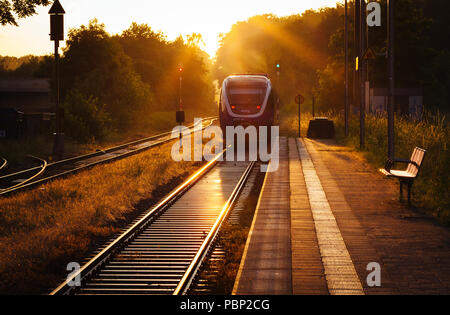 Am späten Nachmittag Sonne spiegelt sich Schienen neben der Plattform wie ein Zug der kleine Bahnhof von Quelle, in der Nähe von Halle (Westfalen), Ge Stockfoto