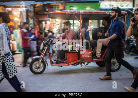 Ein elektrisches Fahrrad Rikscha fahren die Passagiere durch die belebten Straßen von New Delhi an einem heißen Sommerabend. Stockfoto