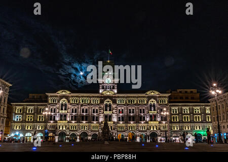 Triest, Italien, vom 28. Juli 2018. Der Vollmond scheint aus den Wolken hinter dem Rathaus von Triest an der Piazza Unità d'Italia. Die Zahlen, die Stockfoto