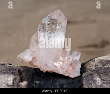 Himalayan klare Quarz Cluster mit Hämatit Einschlüsse auf nassem Sand am Strand bei Sonnenaufgang. Stockfoto