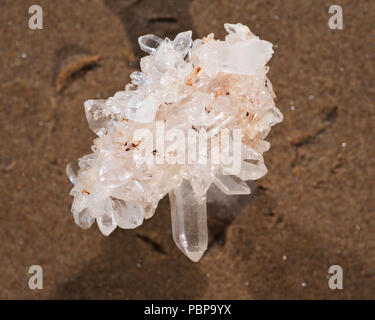 Himalayan klare Quarz Cluster mit Hämatit Einschlüsse auf nassem Sand am Strand bei Sonnenaufgang. Stockfoto