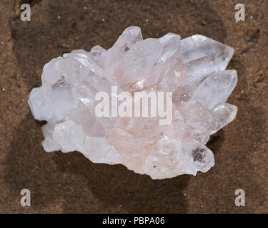 Himalayan klare Quarz Cluster mit Hämatit Einschlüsse auf nassem Sand am Strand bei Sonnenaufgang. Stockfoto