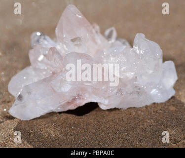 Himalayan klare Quarz Cluster mit Hämatit Einschlüsse auf nassem Sand am Strand bei Sonnenaufgang. Stockfoto