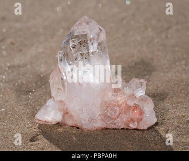 Himalayan klare Quarz Cluster mit Hämatit Einschlüsse auf nassem Sand am Strand bei Sonnenaufgang. Stockfoto