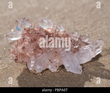 Himalayan klare Quarz Cluster mit Hämatit Einschlüsse auf nassem Sand am Strand bei Sonnenaufgang. Stockfoto