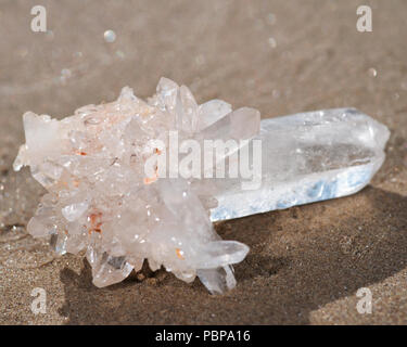 Himalayan klare Quarz Cluster mit Hämatit Einschlüsse auf nassem Sand am Strand bei Sonnenaufgang. Stockfoto