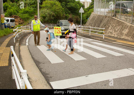 CHATAN STADT, Okinawa, Japan - 1. Sgt. Abelardo V. Dominguez stoppt Verkehr für Kinder und ihre Mutter auf dem Weg zur Kitatama Volksschule Juli 19 in Chatan Stadt, Okinawa, Japan. Dominguez freiwillig als Crossing Guard, um zu helfen, die Volksschule, die Sicherheit der Kinder sorgen, als Sie zu Fuß entlang der geschäftigen Straßen von chatan Stadt zur Schule. Dominguez ist Sergeant Major von Camp Foster und Sitz und Unterstützung Bataillon, Marine Corps Installationen Pacific-Marine Corps Base Camp Butler, Japan. (U.S. Marine Corps Foto von Cpl. Danielle R. Prentice) Stockfoto