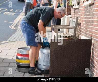 Ein Mann senken Kegs (Fässer, Fässer) Alkohol (Bier?) durch eine Luke in den Keller einer Kneipe in West Sussex, England, UK. Alkohol Lieferung. Stockfoto