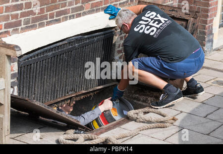 Ein Mann senken Kegs (Fässer, Fässer) Alkohol (Bier?) durch eine Luke in den Keller einer Kneipe in West Sussex, England, UK. Alkohol Lieferung. Stockfoto