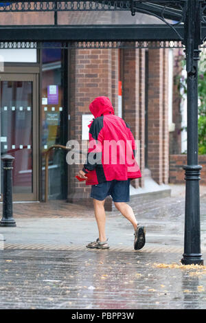 North Wales, 29. Juli 2018. UK Wetter: Die ersten echten nachhaltigen Niederschlag für viele heute einschließlich Flintshire, das ist eine willkommene Abwechslung von der jüngsten Hitzewelle. Ein Mann stürzte durch den Regen tragen eine Regenjacke für den Schutz gegen die schweren Regen in der Marktgemeinde Schimmel, Flintshire, Wales Stockfoto