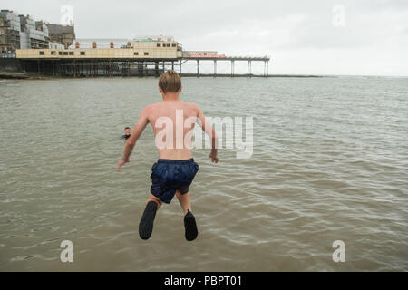 Aberystwyth Wales UK, Sonntag, den 29. Juli 2018 UK Wetter: Jugendliche immer noch Spaß haben einen Sprung von der Anlegestelle, obwohl es ein grau, nass und bedeckt Sonntag am Meer in Aberystwyth auf der West Wales Küste der langen Hitzewelle schließlich bricht mit Gewitter und sintflutartige Regenfälle über viel des Landes Foto: Keith Morris/Alamy leben Nachrichten Stockfoto