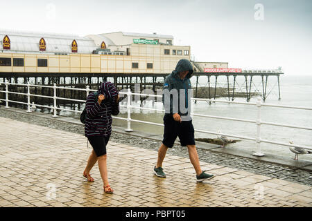 Aberystwyth Wales UK, Sonntag, den 29. Juli 2018 UK Wetter: Leute auf einem grauen, nassen und bedeckt Sonntag getränkt am Meer in Aberystwyth auf der West Wales Küste. Die langen Hitzewelle bricht schließlich unten mit Gewitter und sintflutartige Regenfälle über viel des Landes Foto: Keith Morris/Alamy leben Nachrichten Stockfoto